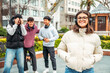 © Nanci - young people having fun together outdoors, a smiling student is listening to music with headphones, her three friends in the background