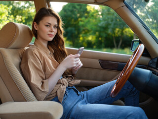 Wall Mural - Young woman texting in a vintage car, wearing casual outfit, exuding relaxed vibes in a lush green setting, ideal for lifestyle and travel themes.