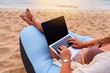 © Goffkein - Black blank empty computer. Nomad girl freelancer lies on inflatable sofa on sandy beach at sunset and typing on a laptop keyboard. Dream job anywhere in the world, distance work