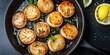 © Rufat - Pan-seared scallops arranged in a skillet with lemon slices on a dark background garnished with herbs and a buttery sauce glistening