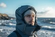 © Vitalii Shkurko - A man stands on the seashore, wearing a windproof hat and warm jacket, gazing at the ocean waves. The cool breeze sweeps across the beach, highlighting a tranquil atmosphere