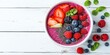 © Levan - Vibrant acai smoothie bowl top view with strawberries blueberries raspberries and chia seeds on white wooden background with ample space for text