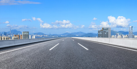 Wall Mural - empty road leading to city skyline and distant hills on a sunny day