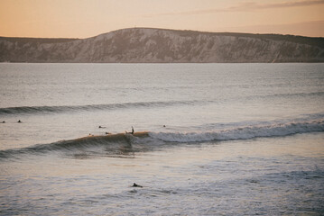 A surfer is riding a wave in the ocean. The water is calm and the sky is orange