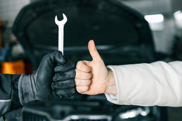 Aufkleber - Close-up of a mechanic's gloved hand holding a wrench and a customer's hand giving a thumbs-up, symbolizing satisfaction and trust in car repair services