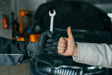 Aufkleber - Close-up of a mechanic's gloved hand holding a wrench and a customer's hand giving a thumbs-up, symbolizing satisfaction and trust in car repair services