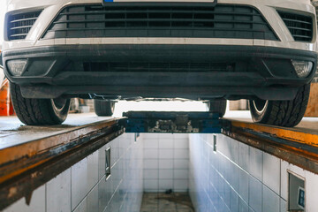 Aufkleber - View of a car positioned over a service pit in an auto repair shop, ready for inspection or maintenance. The focus is on the front bumper and undercarriage area
