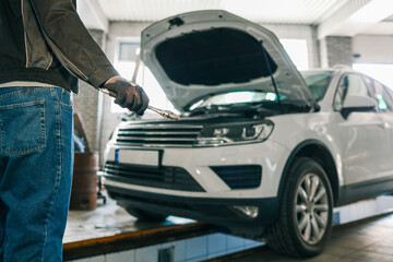 Aufkleber - Mechanic holding an adjustable wrench in a workshop. A white car with its hood open is visible in the background, indicating repair or maintenance work