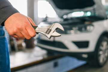 Aufkleber - Mechanic holding an adjustable wrench in a workshop. A white car with its hood open is visible in the background, indicating repair or maintenance work