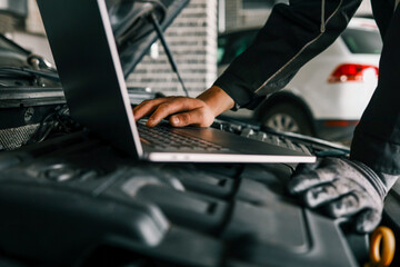 Fototapete - A mechanic using a laptop on a car engine for diagnostics in a garage. Highlights the use of technology in modern vehicle maintenance and repair