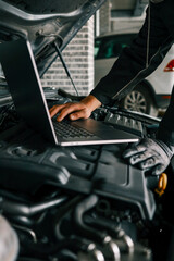 Fototapete - A mechanic using a laptop on a car engine for diagnostics in a garage. Highlights the use of technology in modern vehicle maintenance and repair
