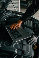Fototapete - A mechanic using a laptop on a car engine for diagnostics in a garage. Highlights the use of technology in modern vehicle maintenance and repair