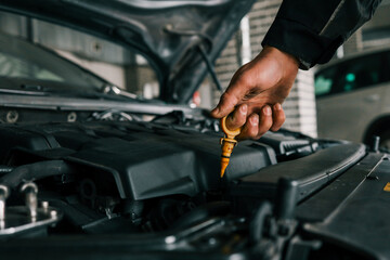 Fototapete - Close-up of a mechanic's hand holding an oil dipstick, checking engine oil levels in a vehicle's open hood. Represents routine car maintenance and servicing