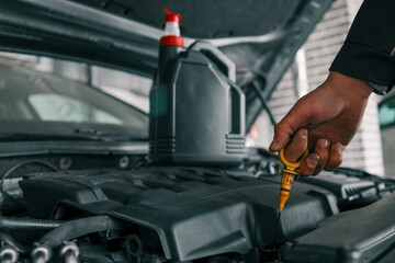 Fototapete - Close-up of a mechanic holding a bottle of motor oil and an oil dipstick, performing an oil change in a vehicle. Highlights car maintenance and servicing tasks