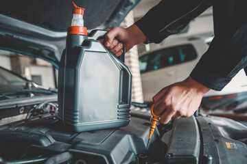 Fototapete - Close-up of a mechanic holding a bottle of motor oil and an oil dipstick, performing an oil change in a vehicle. Highlights car maintenance and servicing tasks