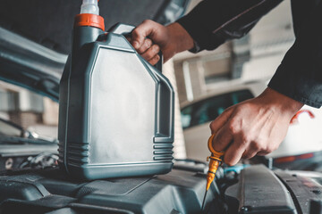 Fototapete - Close-up of a mechanic holding a bottle of motor oil and an oil dipstick, performing an oil change in a vehicle. Highlights car maintenance and servicing tasks