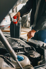 Fototapete - Close-up of a mechanic holding a bottle of motor oil and an oil dipstick, performing an oil change in a vehicle. Highlights car maintenance and servicing tasks