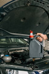 Fototapete - Close-up of a mechanic holding a bottle of motor oil and an oil dipstick, performing an oil change in a vehicle. Highlights car maintenance and servicing tasks