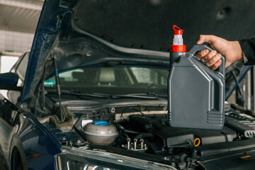Fototapete - Close-up of a mechanic holding a bottle of motor oil and an oil dipstick, performing an oil change in a vehicle. Highlights car maintenance and servicing tasks
