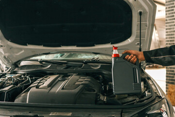 Fototapete - Close-up of a mechanic holding a bottle of motor oil and an oil dipstick, performing an oil change in a vehicle. Highlights car maintenance and servicing tasks