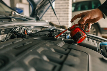Aufkleber - Mechanic using a red oil can to lubricate a vehicle's engine components during routine maintenance in a workshop