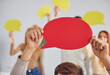 © Studio Romantic - Unrecognizable person showing a paper speech cloud. Cropped shot of a man holding a red mock up message bubble card, with a crowd of other people holding yellow bubbles in the background