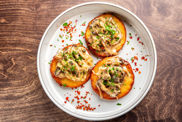 Wall Mural - Deliciously plated mini savory cakes topped with sautéed mushrooms and onions, garnished with fresh herbs and chili flakes, served in a white dish on a wooden table.