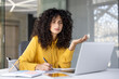 © Liubomir - Serious worried woman at online business meeting conference writing data in notebook. Businesswoman at workplace inside office using laptop for video call.