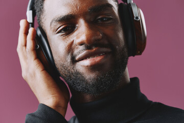 Smiling young Black man enjoying music with headphones on, against a vibrant purple background, conveying joy and relaxation in a modern and stylish setting