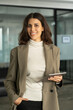 © Stock 4 You - Vertical portrait of 30s beautiful successful hispanic young business woman with tablet pc smiling confident at camera. Latin or eastern middle age female ceo leader businesswoman standing in office.