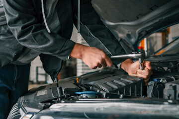 Fototapete - Mechanic tightening a bolt on a car engine using a ratchet wrench in a professional workshop setting