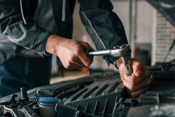 Aufkleber - Mechanic tightening a bolt on a car engine using a ratchet wrench in a professional workshop setting