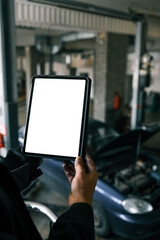 Fototapete - Mechanic holding a tablet with a blank screen in a car repair shop. A blue car with an open hood is in the background, and the workshop has visible car lifts and tools