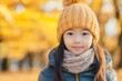 © Mediaphotos - Portrait of smiling girl wearing warm winter clothes. Capturing her cheerful expression amidst an autumn background with yellow leaves and soft sunlight surrounding