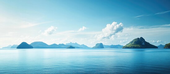 Poster - Panoramic view of tranquil blue ocean with distant mountains and islands under clear sky with scattered clouds Copy Space