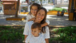 © Krakenimages.com - Woman smiling with her son and daughter outdoors in an urban park, capturing a loving family moment together in a vibrant city setting under bright natural light.