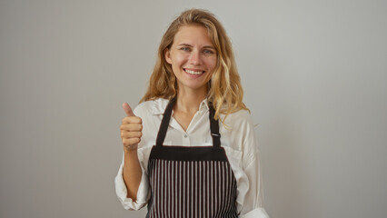 Wall Mural - Woman smiling isolated against a white background shows a thumbs up while wearing a striped apron over a white shirt