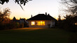 © Pierre Villecourt - Maison de plain-pied en banlieue avec éclairage intérieur chaleureux, grandes fenêtres et pelouse spacieuse au coucher du soleil