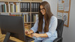 © Krakenimages.com - Woman typing on computer at office desk with bookshelf, corkboard, and documents in background