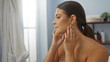 © Krakenimages.com - Young woman with brunette hair in a wellness spa center, checking her skin while sitting in a calm indoor beauty room