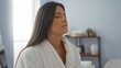 © Krakenimages.com - Beautiful hispanic woman relaxing in a spa room wearing a white robe with her eyes closed, enjoying a peaceful moment indoors
