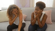 © Krakenimages.com - Women friends sitting together in a living room, conveying mixed emotions and engaging in a deep conversation, showcasing bonds and interactions within a home setting.