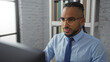 © Krakenimages.com - Young man with braids working on computer in modern office wearing glasses and blue shirt showcasing professional focus in corporate environment with brick wall background