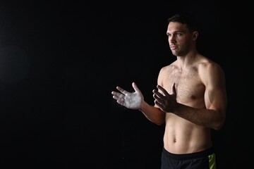 Man clapping hands with talcum powder before training on black background. Space for text