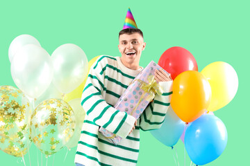 Wall Mural - Young man with gift box and bunches of colorful balloons on green background