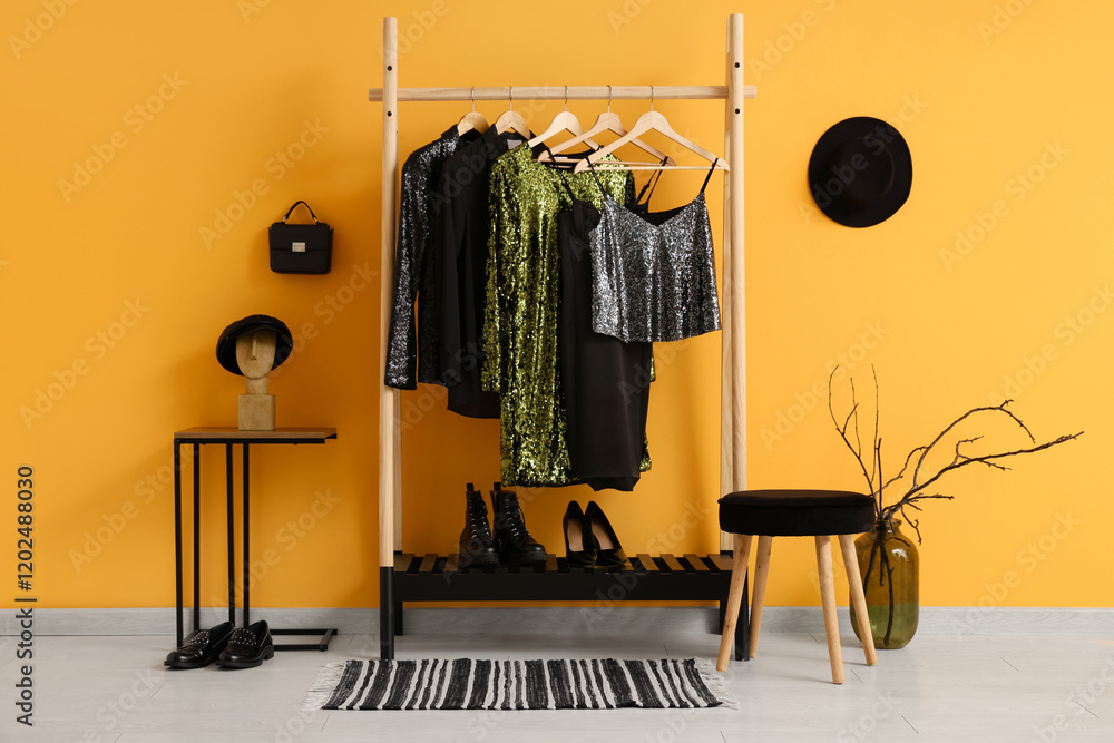 Rack with evening clothes and accessories near yellow wall in dressing room
