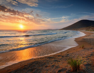 Wall Mural - A golden sun sets over a curved sandy beach with rolling waves while orange clouds paint the sky above a coastal mountain.