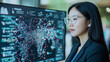 © Kingdola - Data Driven Decisions: A focused young woman wearing glasses gazes intently at a large monitor displaying intricate data visualizations.
