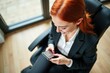 © SimpleDesignStudio - Top View of a Confident Businesswoman in a Black Suit Checking Her Smartphone While Sitting in a Modern Office Chair with Minimalistic Background