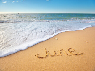 Wall Mural - June word written on sea sand shore beach at day.